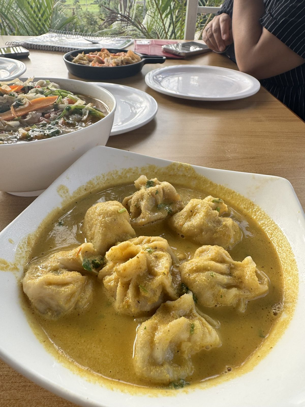Steamed momos in a yellow curry sauce on a square white plate
