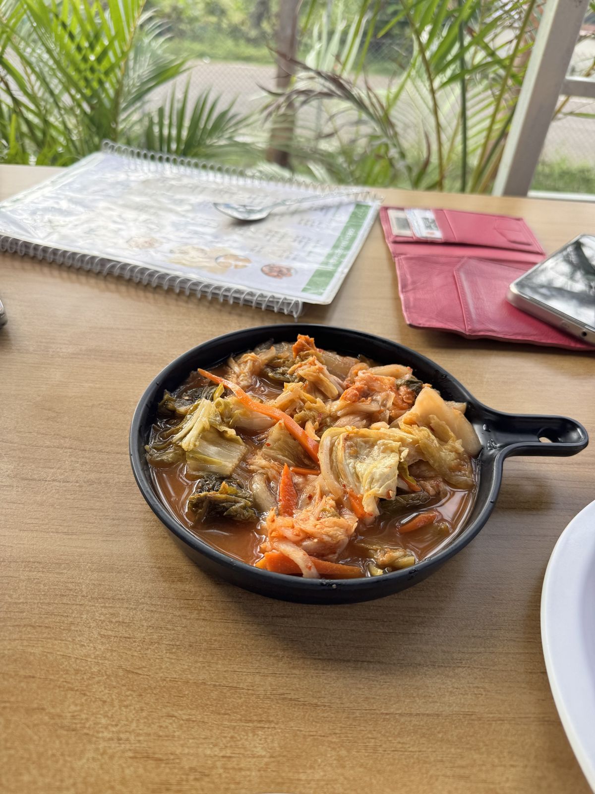 Spicy cabbage and carrot kimchi in a small black pan on a wooden table