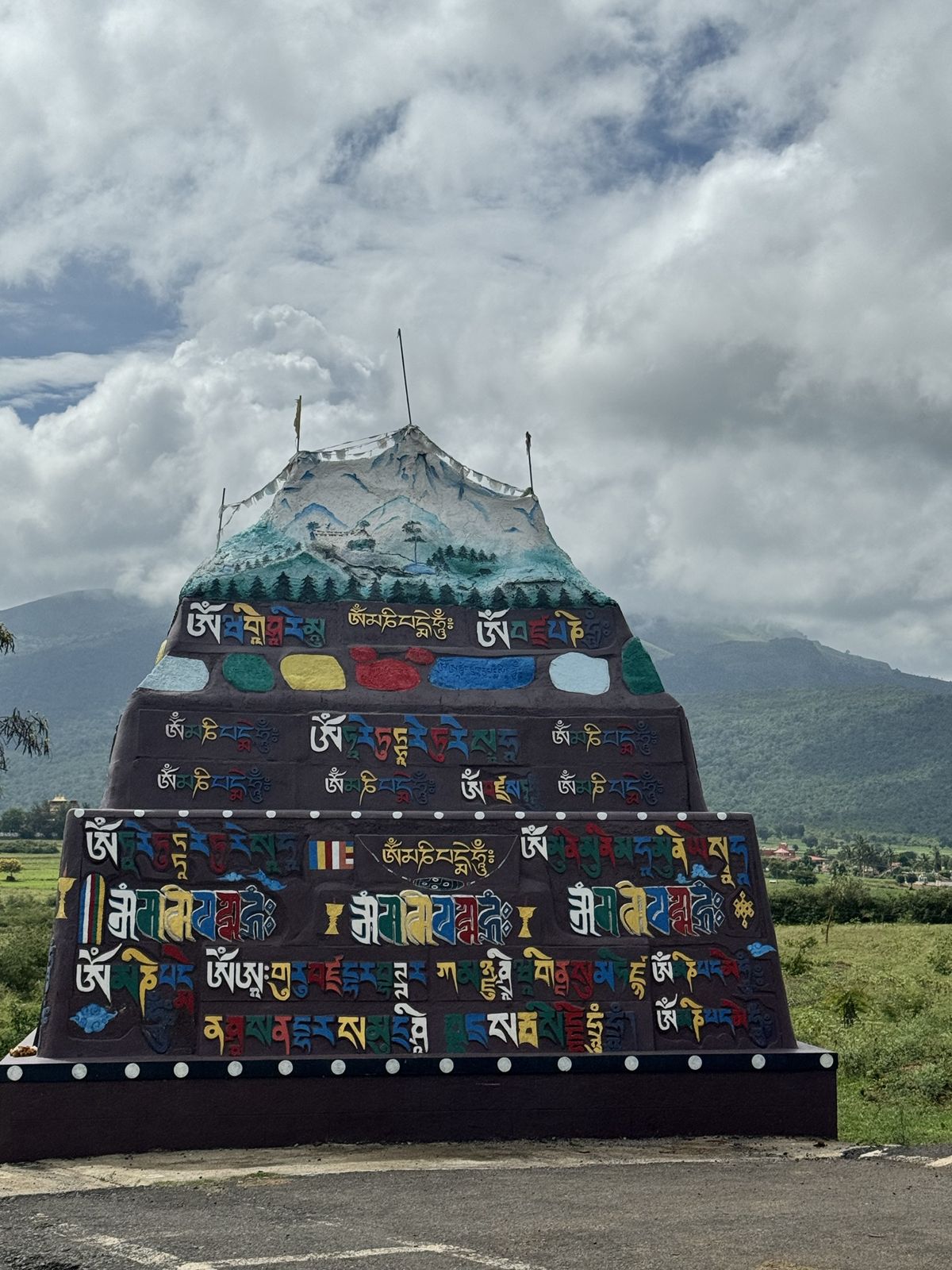 A large painted mound covered in colourful Tibetan mantras, topped with a painted snow mountain and prayer flags