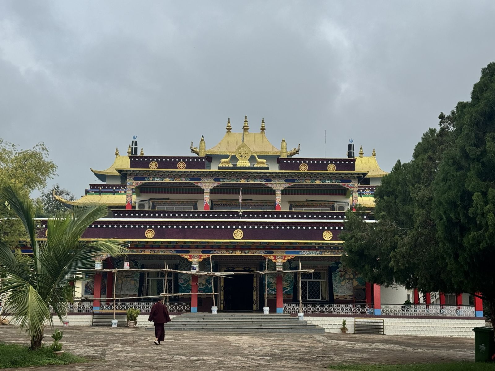 Front of a large Tibetan monastery with golden roofs and colourful painted beams, a monk walking across the courtyard