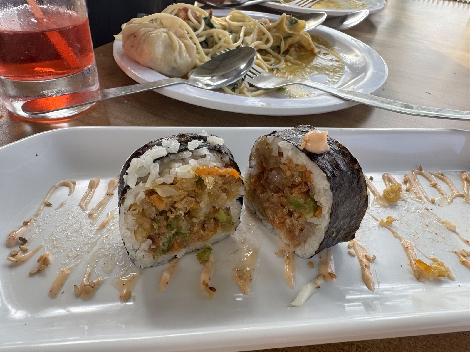 A thick sushi roll cut in half, filled with crispy vegetables, with spicy mayo on the plate